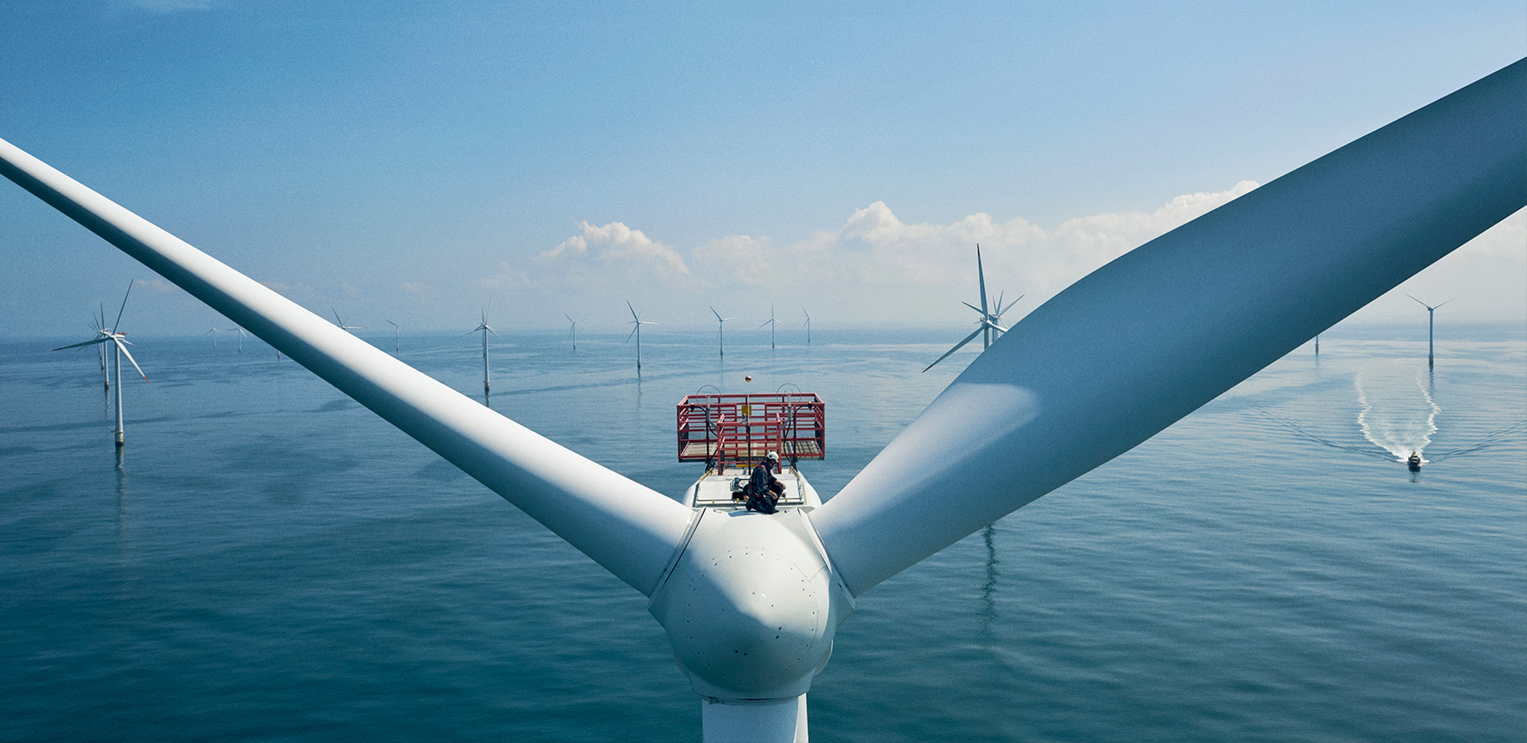A man sits on top of a wind turbine placed in the ocean